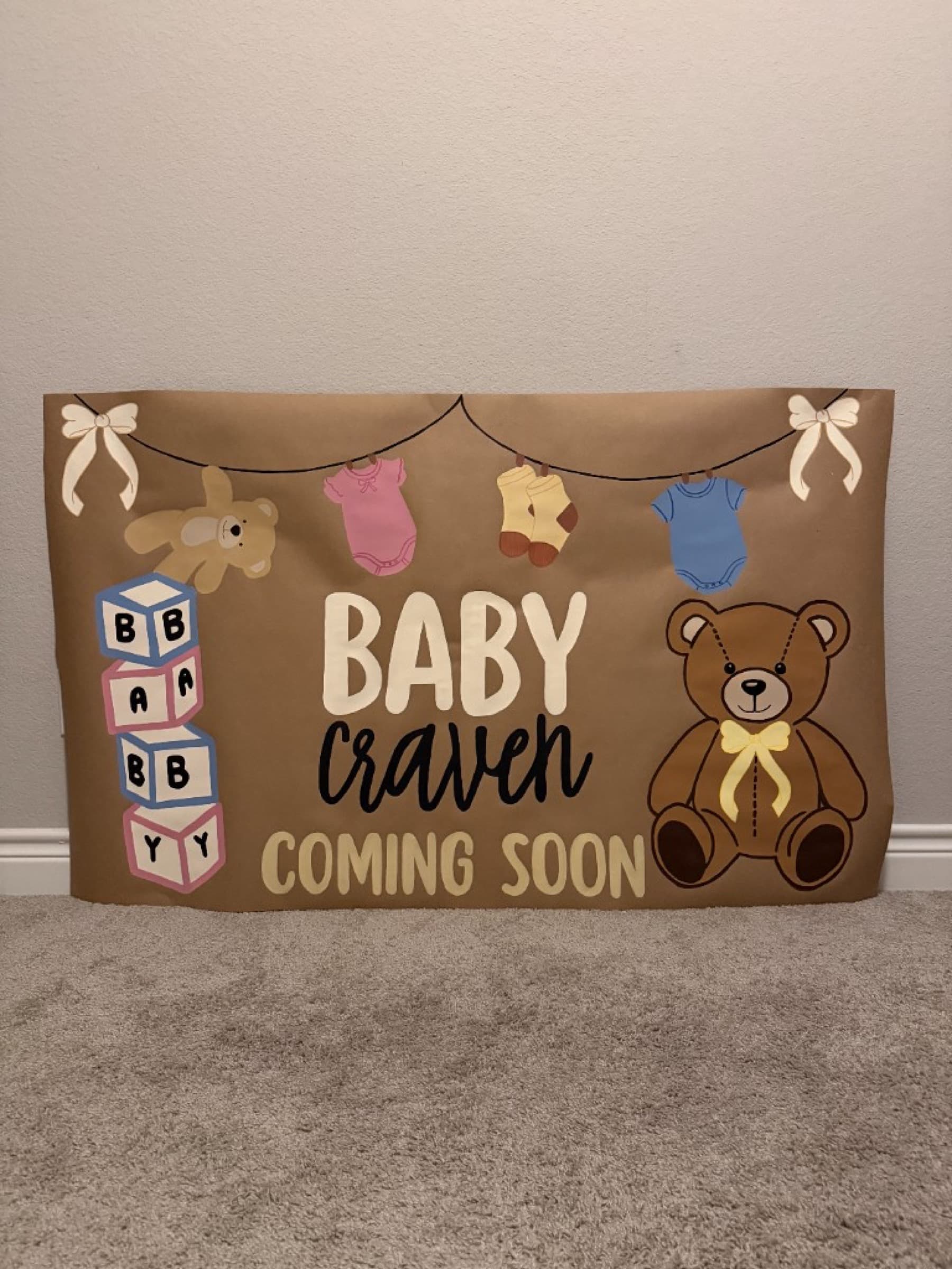 Kraft paper baby banner reading Baby Craven Coming Soon with teddy bears, alphabet blocks, and a clothesline of baby clothes