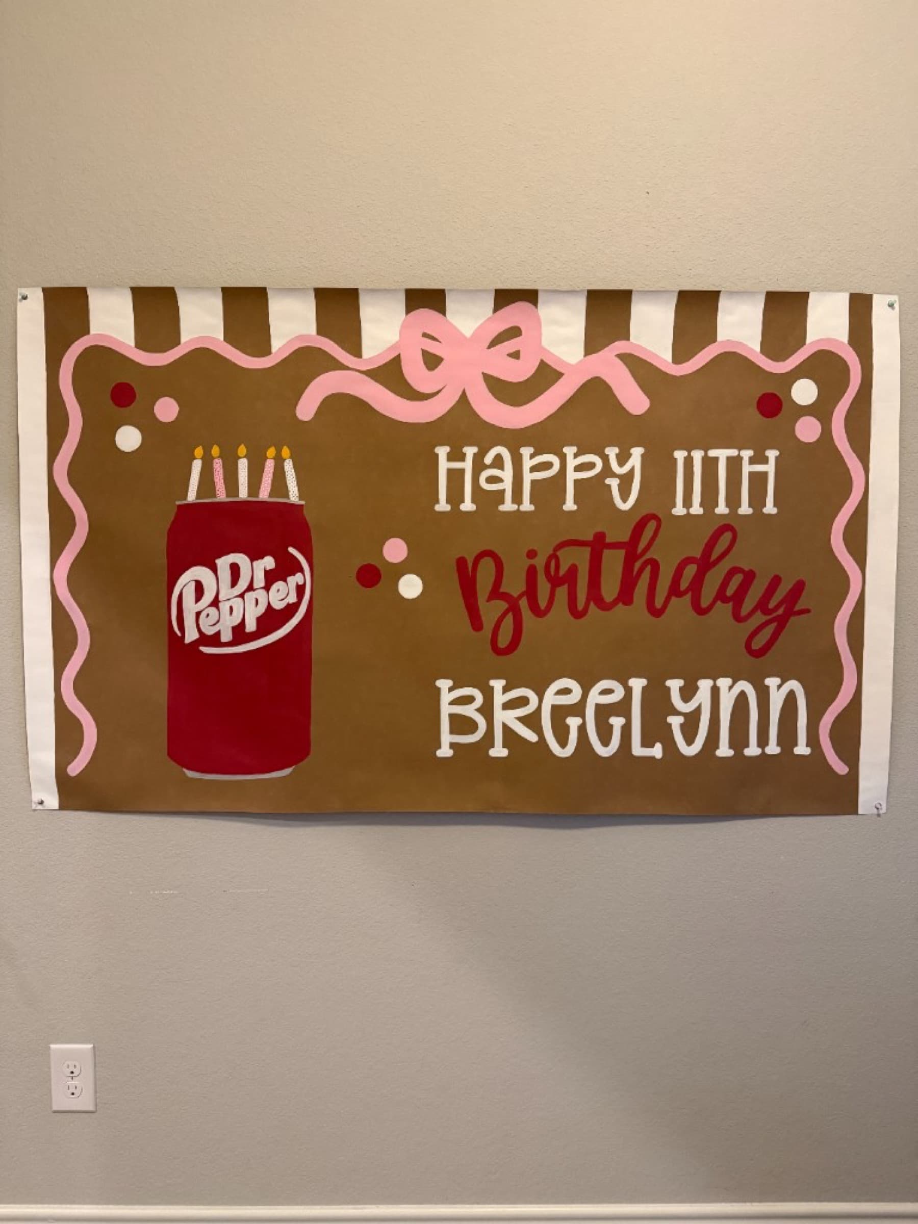 Kraft paper banner reading Happy 11th Birthday Breelynn with a Dr Pepper can, pink bow, and striped top border