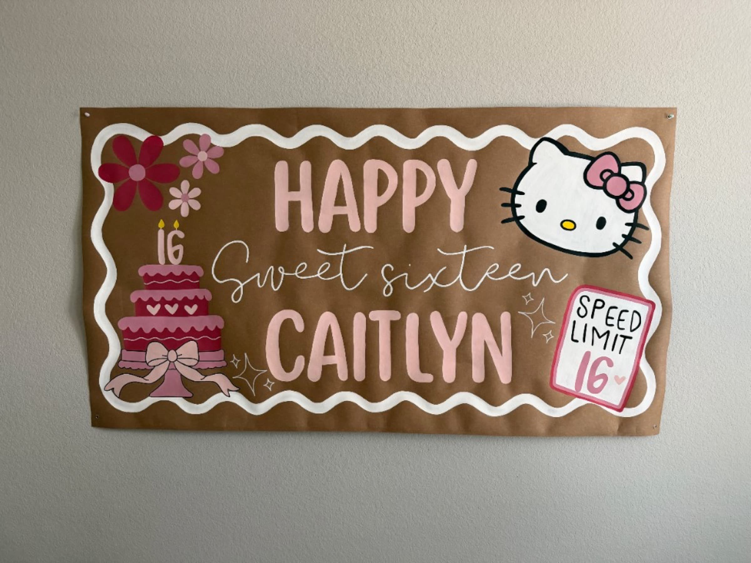 Kraft paper banner reading Happy Sweet Sixteen Caitlyn with Hello Kitty, a pink cake, flowers, and a speed limit 16 sign