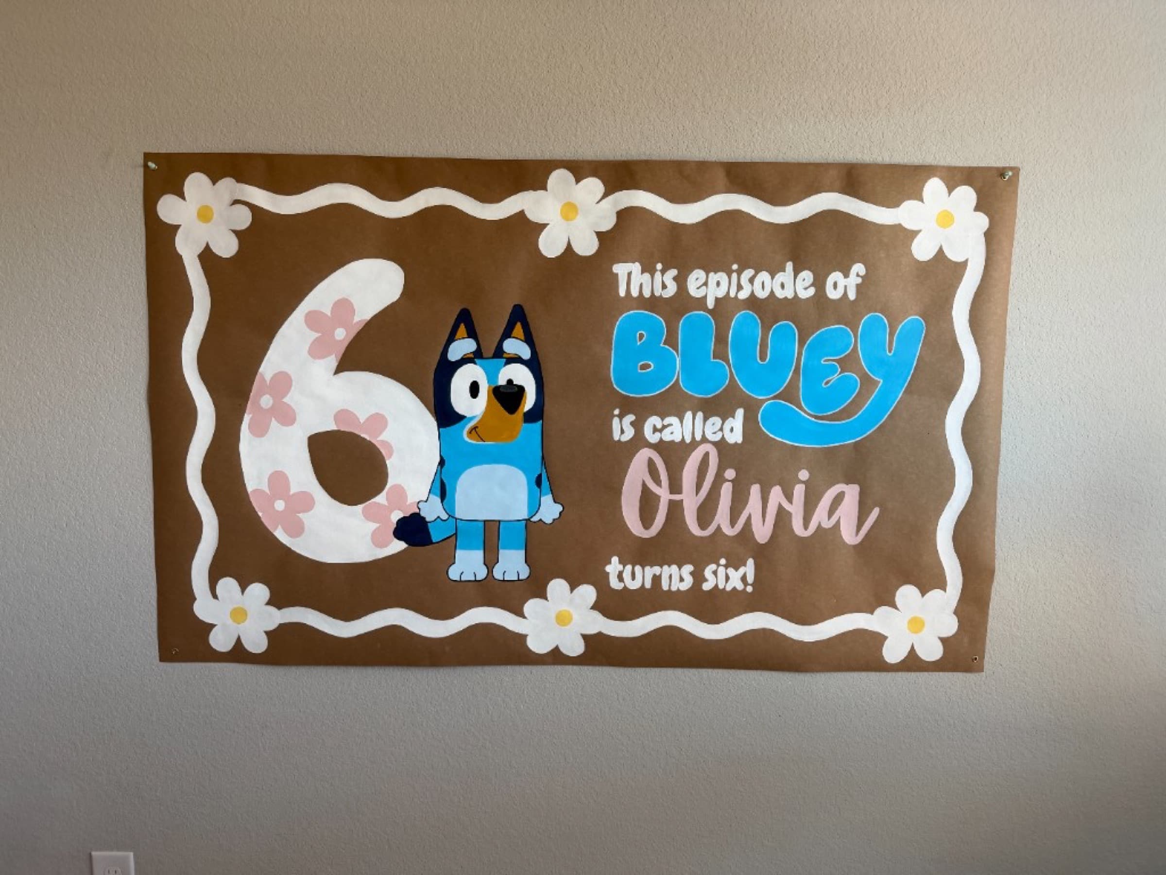 Kraft paper banner reading This episode of Bluey is called Olivia turns six, with a large floral 6 and Bluey in the center